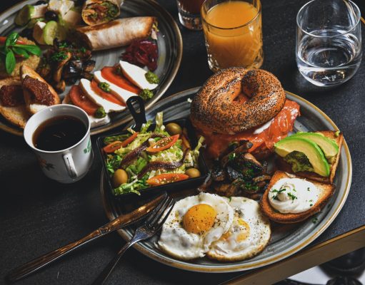 hamburger, fried eggs, avocado slices, and bread on round gray plate